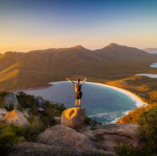 Person standing on a cliff with arms raised overlooking a scenic coastline representing the Explorer archetype of freedom and adventure