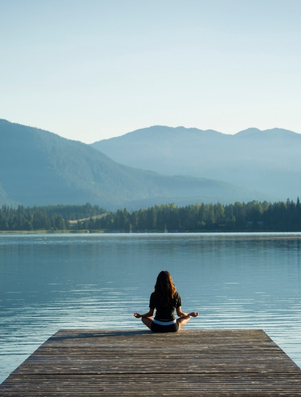 Person meditating by a calm lake with mountains in the background representing natural health and wellness