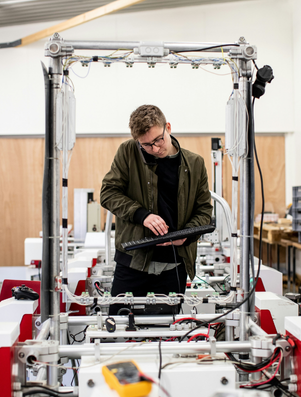 Man working with advanced machinery in a workshop, holding a keyboard and focusing on technology development.