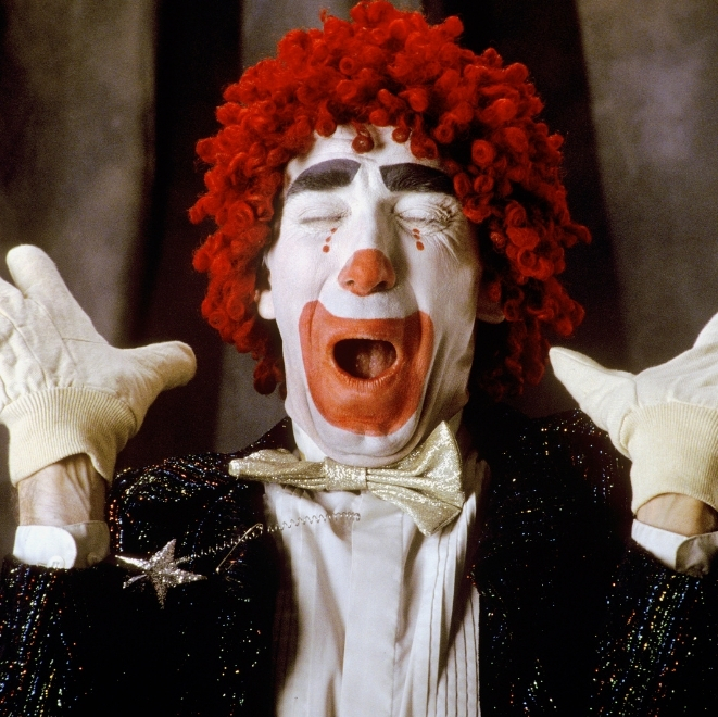 Clown with red wig and white gloves making a playful face representing the Jester archetype of humour and joy