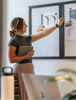 Confident woman presenting ideas on a board in a modern office while colleagues listen attentively.