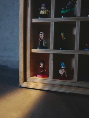 Wooden display case with small figurines arranged in compartments, with a spotlight highlighting one figure at the edge.