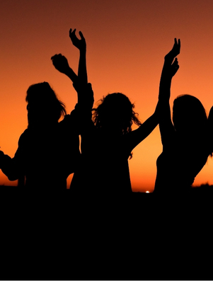 Group of people dancing and laughing in silhouette at sunset representing the Jester archetype of playfulness and joy