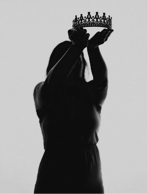 Silhouette of a person holding up a crown with both hands, symbolising honour, leadership, and legacy.
