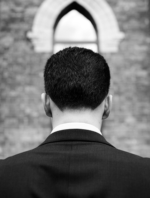 Man in a suit seen from behind, standing before a brick wall with an arched window, symbolising ambition and aspiration.