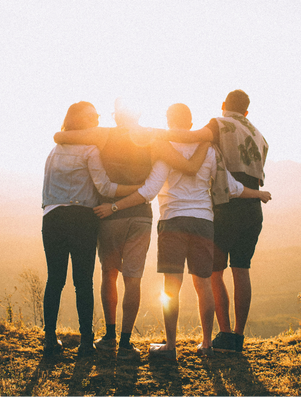 Group of friends standing arm in arm, watching the sunset together on a hilltop.