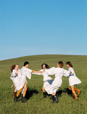 Group of women holding hands and dancing in a field representing the Citizen archetype of unity and belonging