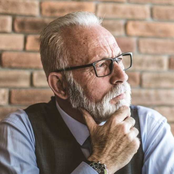 Elderly man with glasses thinking deeply representing the Sage archetype of wisdom and knowledge